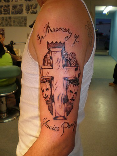 el tatuaje &quoten la memoria de.." con una cruz y dos caras opuestas una alegre y otra triste hecho en el brazo