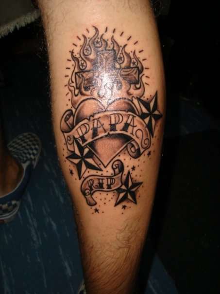 el tatuaje conmemorativo de un corazon,estrellas y una cruz en llamas de fuego hecho en la pierna
