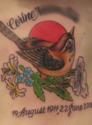 el tatuaje conmemorativo de un gorrion detallado con unas flores y el sol en elfondo, el nombre y fechas de la vida