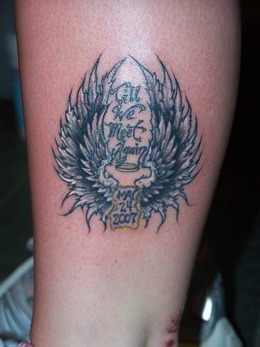 el tatuaje conmemorativo &quotnos volveremos a ver" con una fecha y alas hecho en la pierna