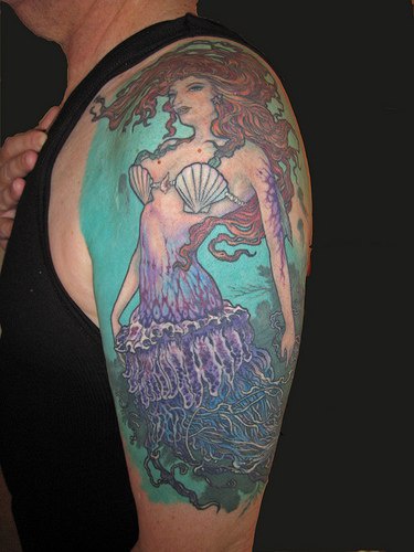 Tatuaggio colorato sul deltoide la sirena sul fondo azzurro
