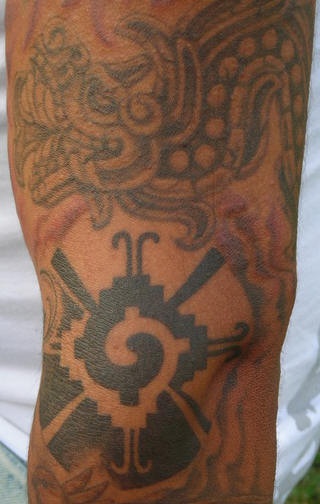 el tatuaje de de un dragon azteca hecho en el brazo con tinta negra y gris