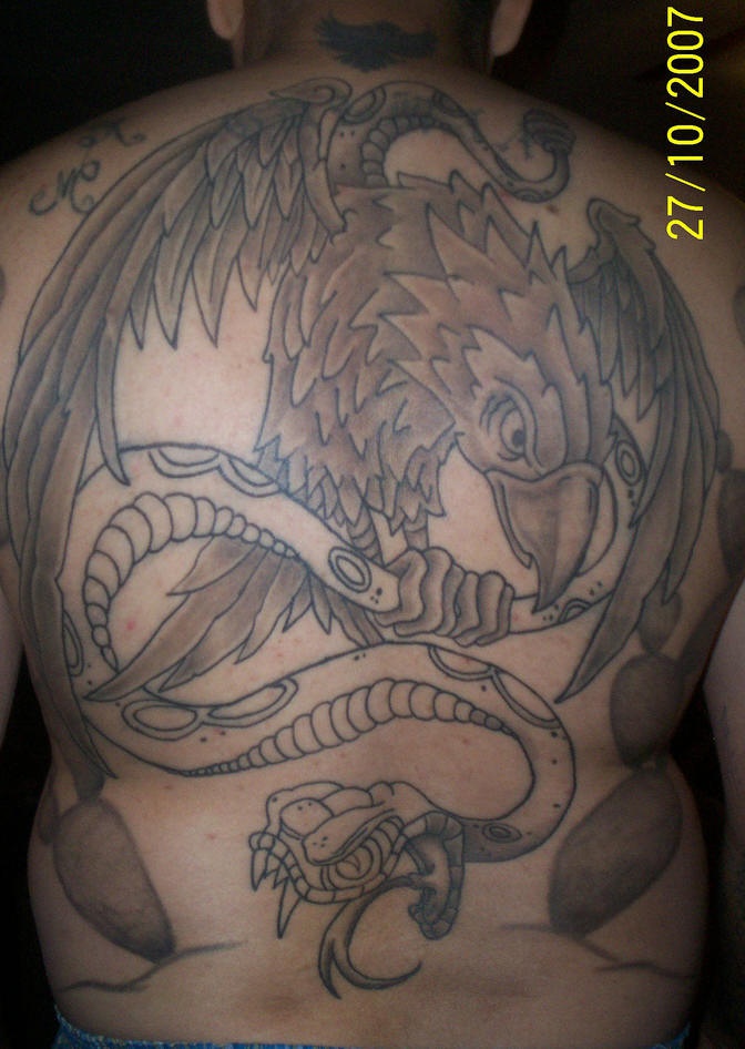 el tatuaje grande de una aguila peleando con una serpiente hecho en toda la espalda