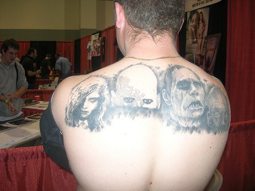 el tatuaje grande de las caras de unos malvados hecho en color negro en la espalda