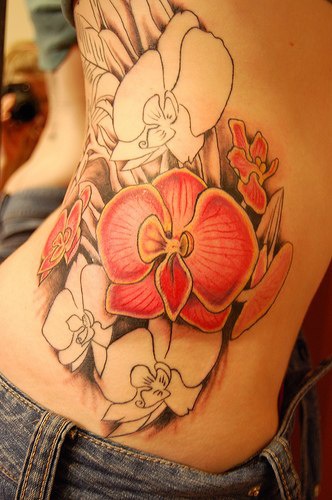 el tatuaje de las orquideas rosas y unas sin colorear hecho en el costado