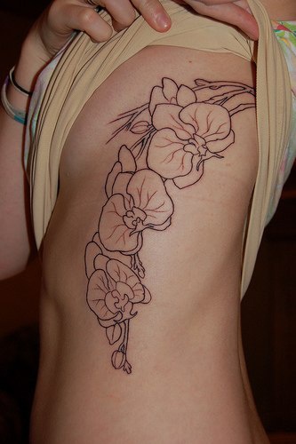 el tatuaje lineado de las orquideas hecho en el costado con tinta negra