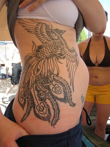 el tatuaje lineado hermoso de la ave magica fenix heho en tinta negra en el costado
