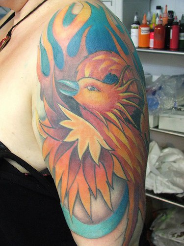 el tatuaje de la ave fenix de color naranja hecho en el hombro