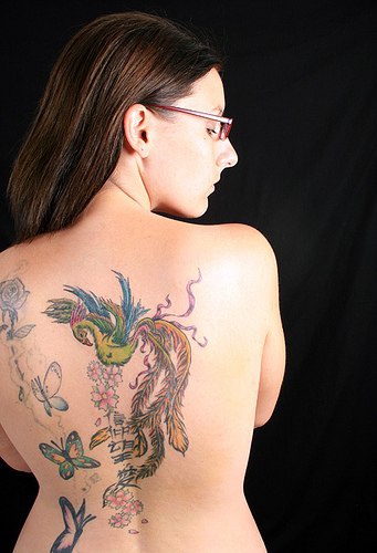 el tatuaje femenino de la ave fenix rodeada de mariposas hecho en la espalda