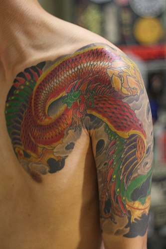 el tatuaje en estilo asiatico de una ave roja hecho en varios colores en el hombro y pecho