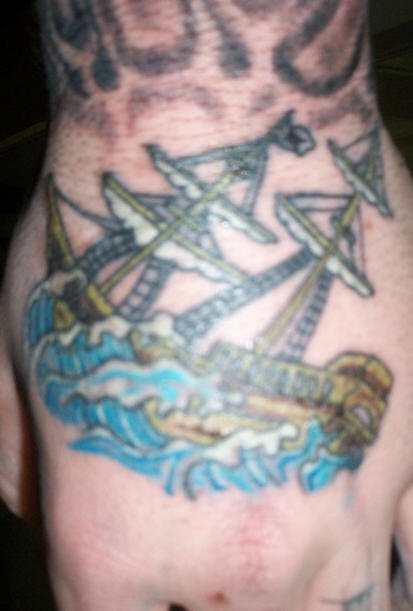el tatuaje pequeño de un barco en el mar hecho en color en la mano
