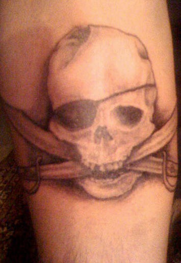 el tatuaje de tinta gris con una calavera pirata con cuchillos cruzados en su boca