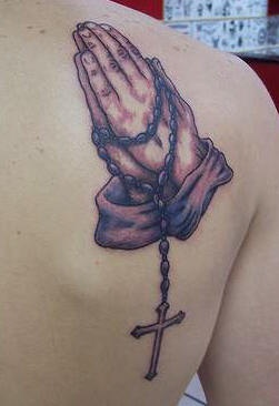 Mani mentre preghiera con rosario tatuaggio sulla spalla