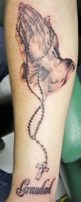 el tatuaje de las manos orantes con rosario hecho en tinta negra