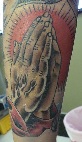 el tatuaje de las manos orantes con el sol rojo en el fondo