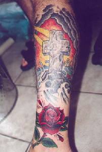el tatuaje colorado de la cruz de piedra con una rosa roja hecho en el brazo