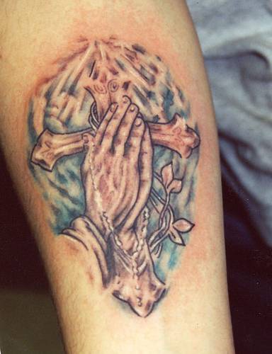 el tatuaje colorado de las manos orantes sobre una cruz