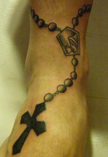 Tatuaje en tinta negra rosario con cruz en el tobillo
