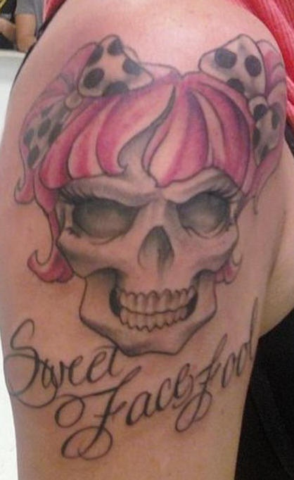 Le tatouage de l"épaule avec la crâne de fille avec des nœuds et une inscription