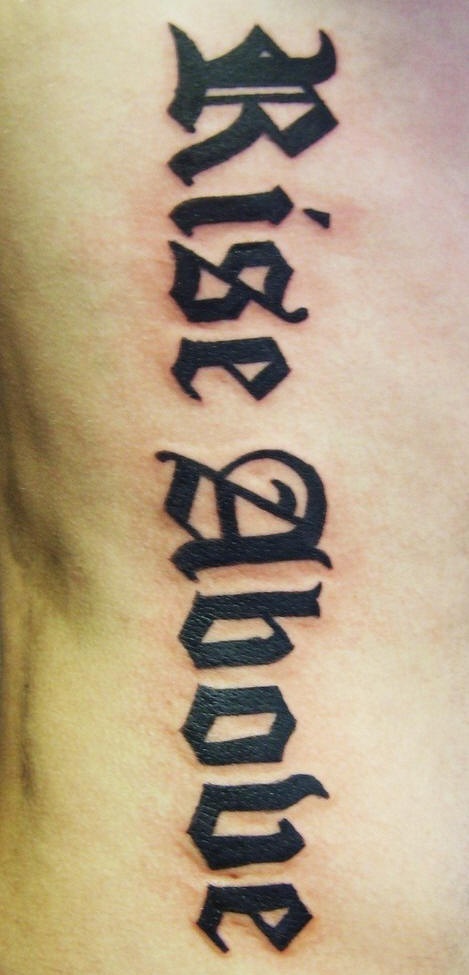 Tatuaggio sul fianco la scritta &quotRISE ABOVE" a lettere calligrafiche