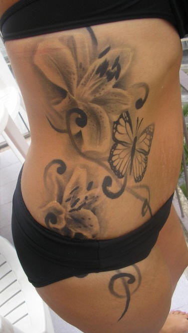 Precioso tatuaje en el costado, flores grandes con mariposa en tinta negra