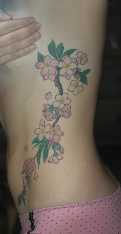 Tatuaggio colorato sul fianco il ramoscello del ciliegio fiorito