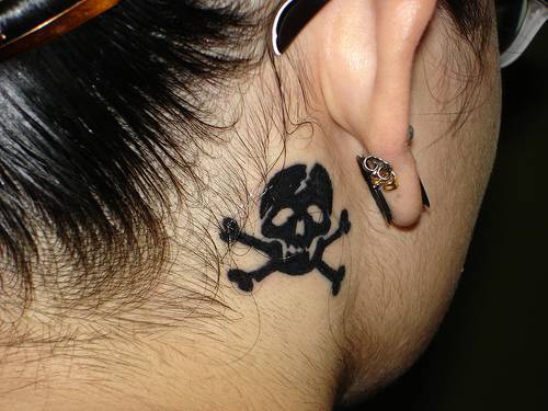Chiquito tatuaje de calavera con los huesos cruzados detrás de la oreja