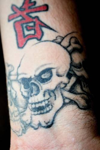 Tatuaje de maligna calavera con los huesos cruzados y jeroglífico rojo