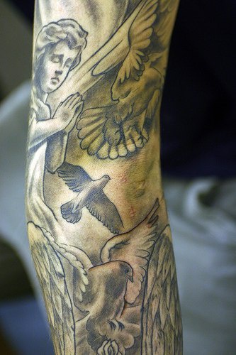 Ángel rezando y unas palomas blancas tatuaje en la manga