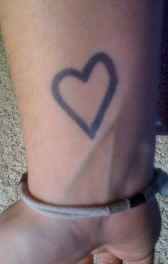 Black ink heart symbol tattoo on wrist