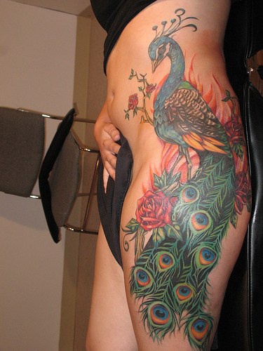 Tatuaje en la cadera, pavo elegante entre flores, abigarrado