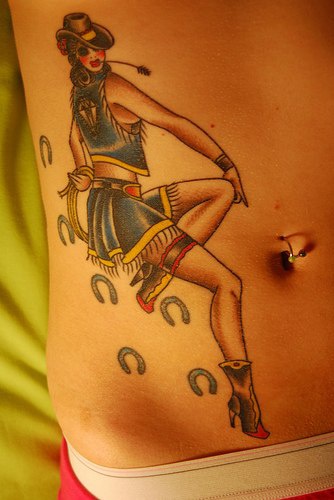Bauch Tattoo von verspielter Cowgirl mit Hut, Stiefeln und vielen Hufeisen