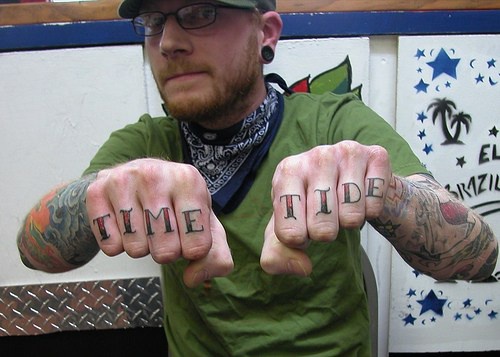Tattoo mit großer farbiger Inschrift &quotTime tide" an Fingerknöcheln