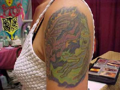 el tatuaje con un alienigena peleando con un demonio hecho en colores en el hombro