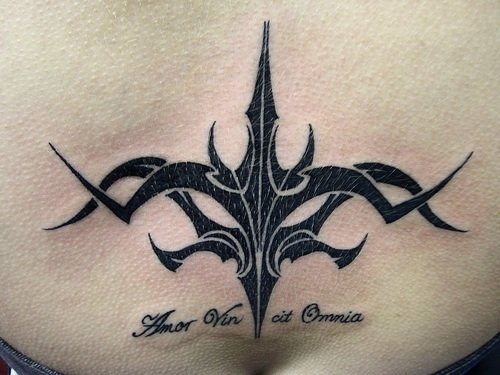 Tatuaje en tinta negra, en bajo de la espalda, estilo tribal, pequeña inscripción