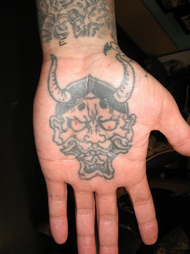 Tatuaje en la palma, demonio con cornudos largos descolorido