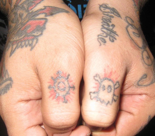 Tattoo mit Sonne- und Totenkopfzeichen an Daumenknöcheln