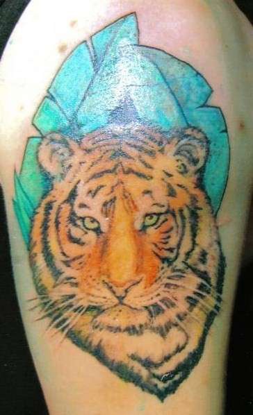 Cabeza del tigre al fondo de las hojas verdes tatuaje en el hombro