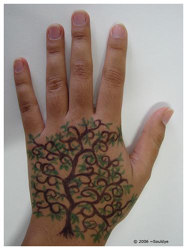 Hand tattoo of brown tree with green leaves