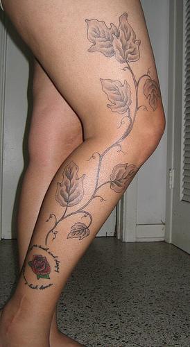 Un long arbre avec des gros feuilles le tatouage sur la jambe