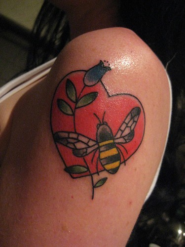 el tatuaje de un corazon rojo con una flor y una abeja hecho en el hombro