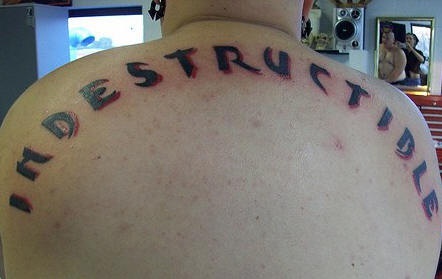 Indestructible on upper back black inscription tattoo