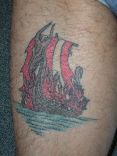 Pequeño tatuaje en color la nave  de los vikings en el fuego