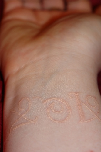 White ink tattoo with year on wrist