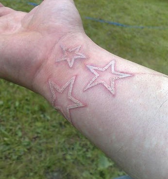 White ink tattoo with three stars on wrist
