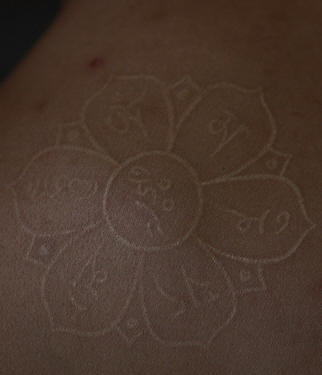 Tatuaje la flor con los símbolos de yoga en tinta blanca