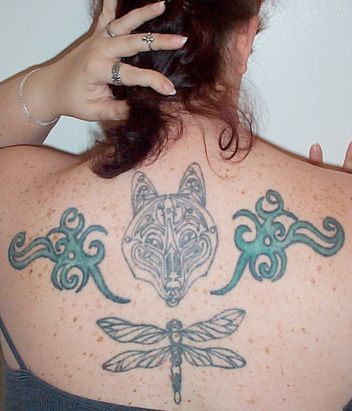 Big tattoo on back with wolf head, blue signs and dragonfly