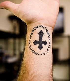 Tatuaggio sul polso la croce nera con la scritta attorno