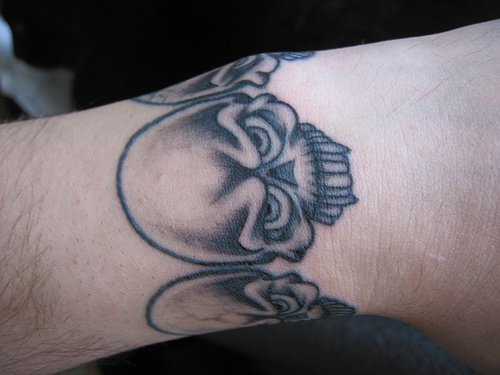 Le tatouage bracelet de poignet avec des grosse crânes