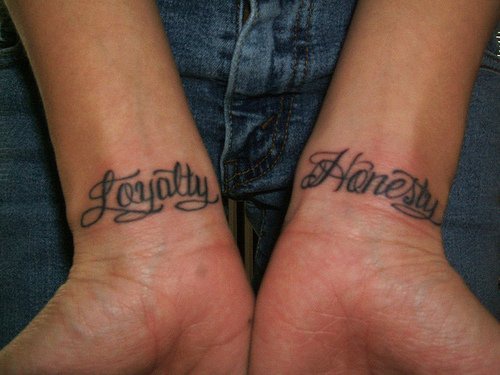 Calligraphic tattoo with words Loyalty and Honesty on both wrists